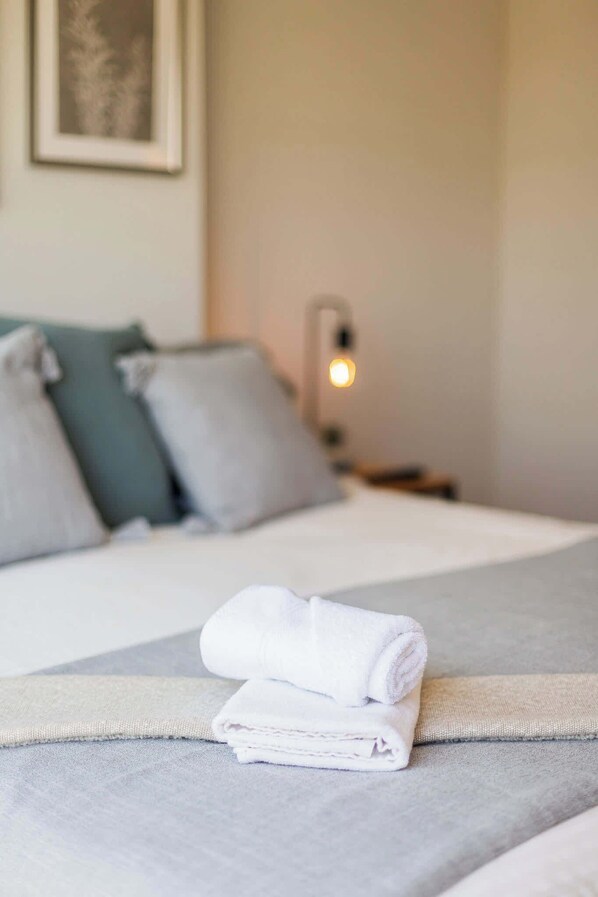 A neatly made bed with a folded white towel, a gray blanket, and two pillows. - Chic Urban Studio Perfect for Business or Leisure (Ñuñoa)
