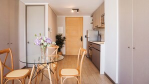 A compact kitchen with a dining area, featuring a glass table and wooden chairs, a wooden door, and a small refrigerator. - Chic Urban Studio Perfect for Business or Leisure (Ñuñoa)