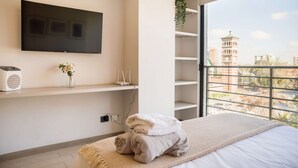 A modern bedroom with a large TV, a plant, and a view of a cityscape. - Chic Urban Studio Perfect for Business or Leisure (Ñuñoa)