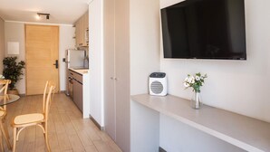A compact living space with a kitchenette, a dining area with a table and chairs, a mounted flat-screen TV, a portable heater, and a vase with flowers. - Chic Urban Studio Perfect for Business or Leisure (Ñuñoa)