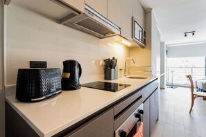 Modern studio kitchen with a sleek induction cooktop, built-in appliances, and a bright open-plan dining area beyond. - Comfortable Studio Apartment in Nunoa Ideal for 2 (Ñuñoa)