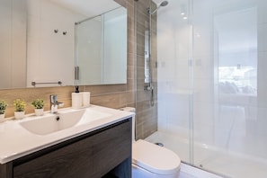 Modern private bathroom with a spacious glass-enclosed walk-in shower, sleek vanity, and warm wood-look tile accents. - Comfortable Studio Apartment in Nunoa Ideal for 2 (Ñuñoa)