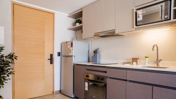 A modern kitchen with a built-in oven, microwave, and a stainless steel sink. - Chic Urban Studio Perfect for Business or Leisure (Ñuñoa)