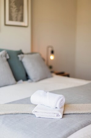 Private bedroom with crisp white bedding, teal accent pillows, and neatly rolled towels on a soft gray throw. - Comfortable Studio Apartment in Nunoa Ideal for 2 (Ñuñoa)