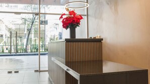 Un espace d’accueil avec un comptoir en bois, une plante rouge en pot et trois luminaires circulaires.