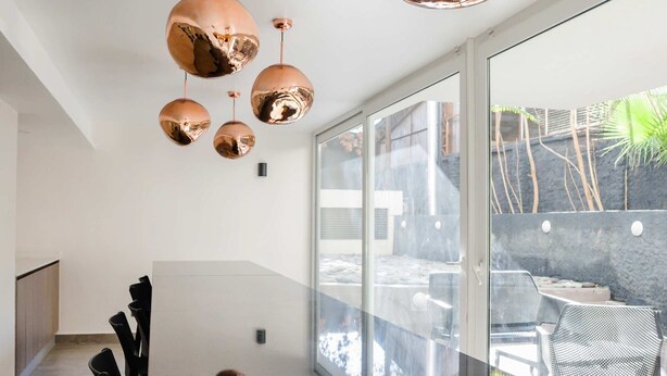 Une cuisine moderne dotée d’un grand îlot central, de luminaires suspendus en cuivre et offrant une vue sur la terrasse extérieure.