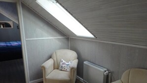 A small, cozy room with a sloped ceiling and a skylight. There is a single chair with a cushion and a small ottoman. - Hotel Miramar  (Dahme)