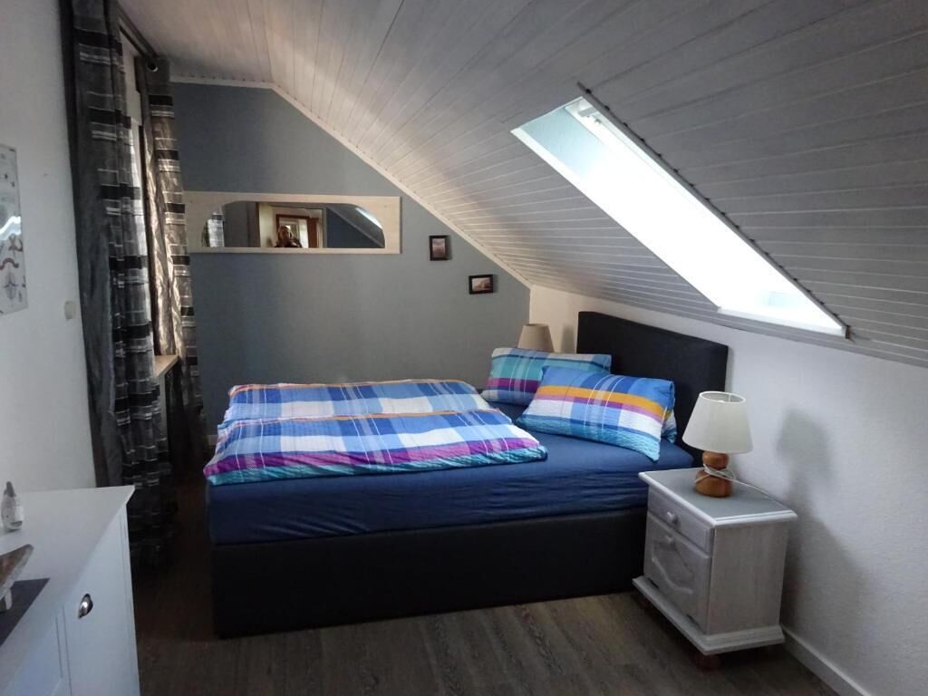 Un dormitorio con cama, mesita de noche con lámpara, tragaluz y espejo en la pared.
