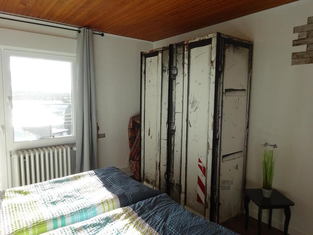 A bedroom with a bed, a radiator, a window, a wardrobe, and a small table with a plant.