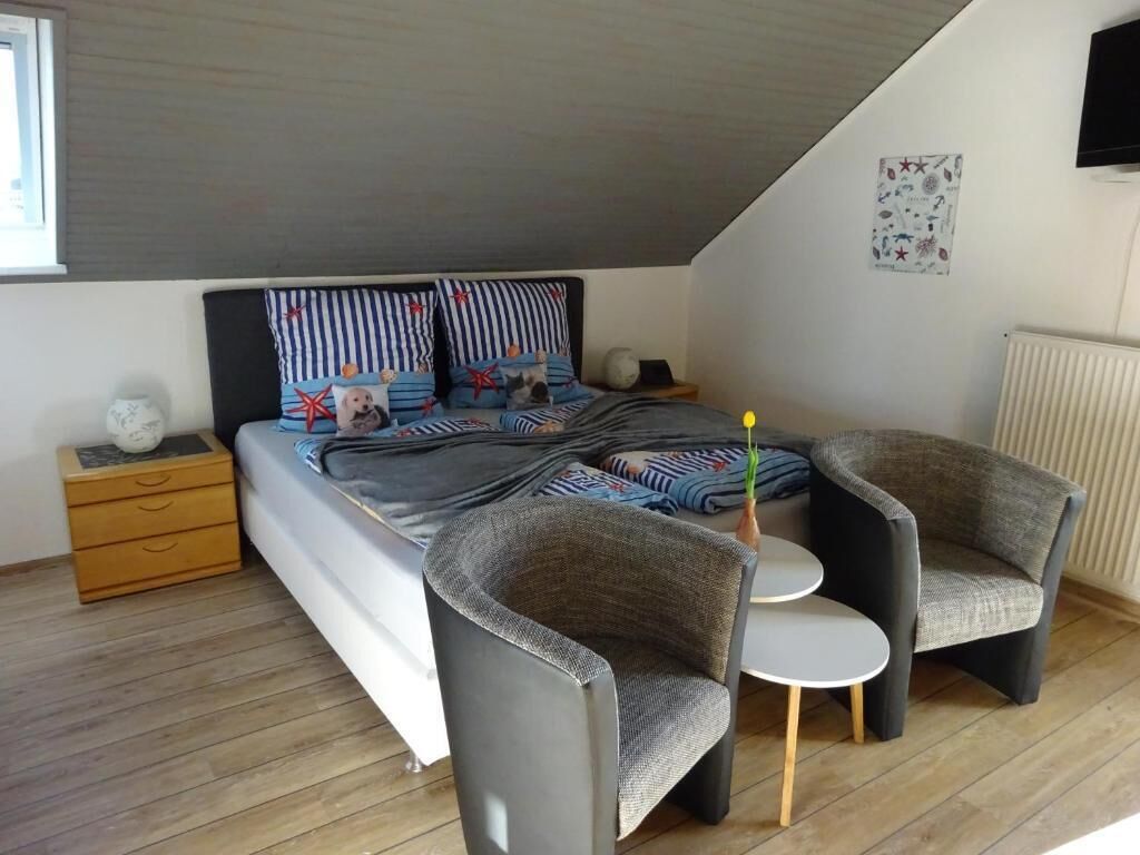 Ett modernt sovrum med en säng, två fåtöljer, ett litet bord och ett nattduksbord.