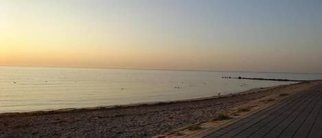 A paved walkway along a beach with a calm sea and a clear sky.