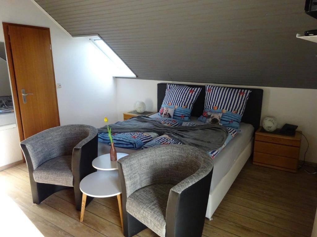 A bedroom with a bed, two armchairs, a small table, and a nightstand.