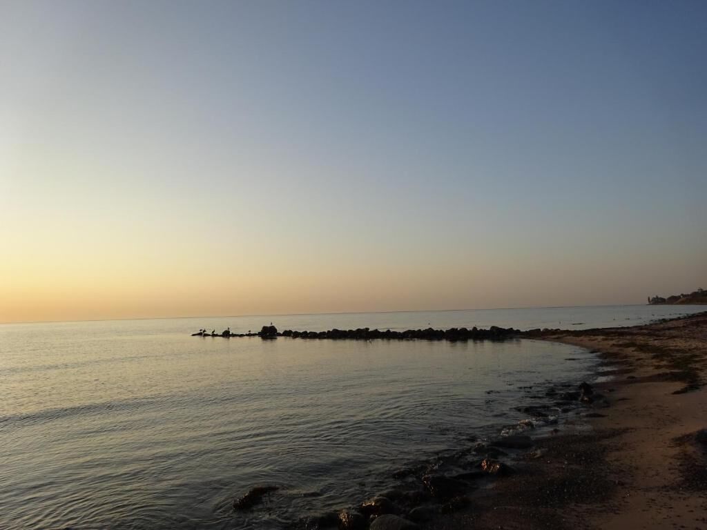 A beach with calm waters, a sandy shore, and a distant rocky outcrop.