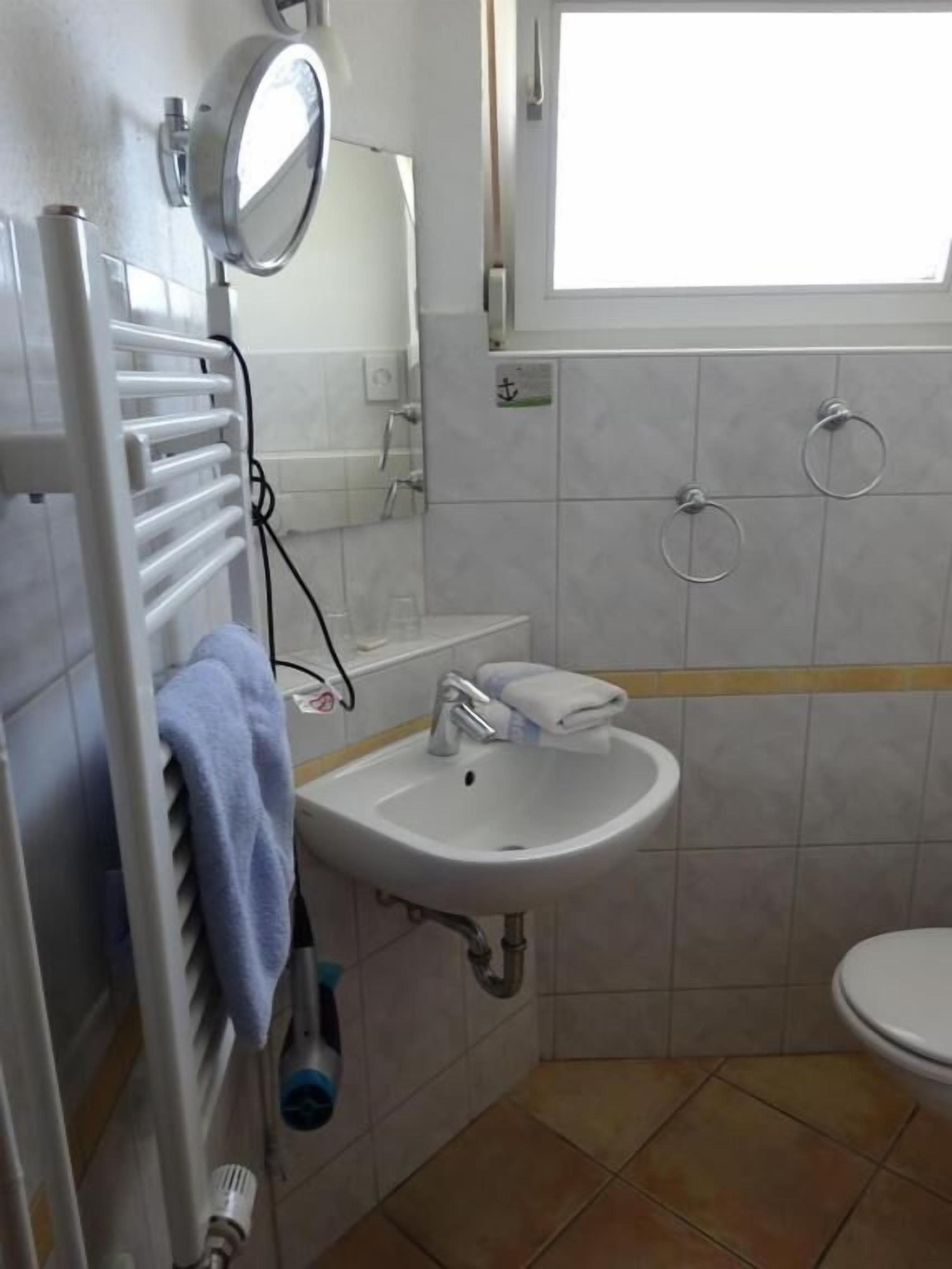 Et badeværelse med en hvid vask, et spejl, et håndklædestativ og et toilet.