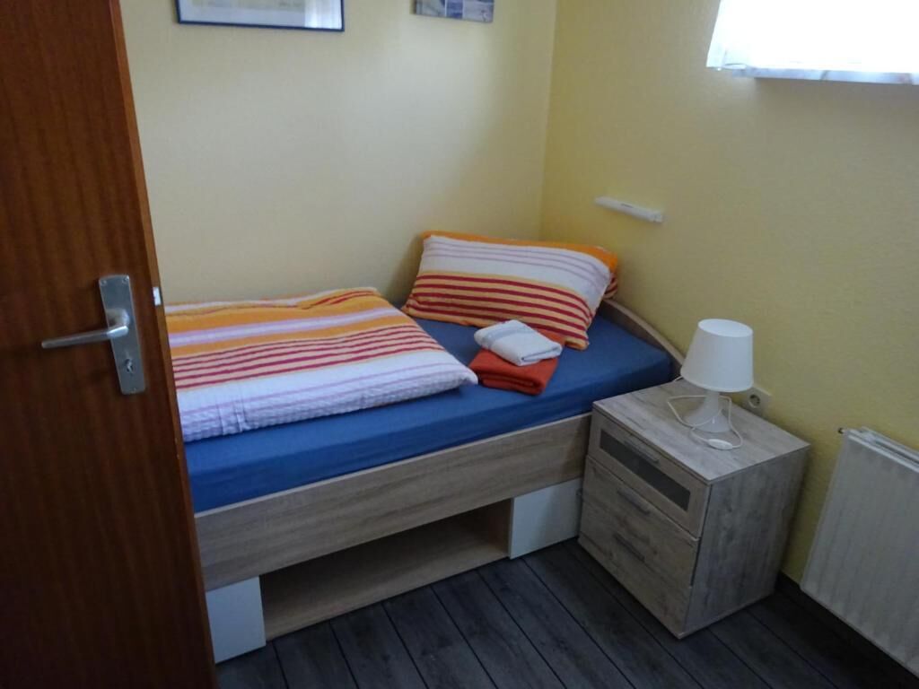 A small, single-bed room with a wooden headboard, a bedside table with a lamp, and a radiator on the wall.