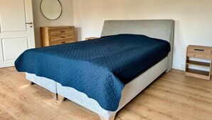 Ein Schlafzimmer mit einem Bett, einem Schminktisch, einem Nachttisch und einem runden Spiegel an der Wand.