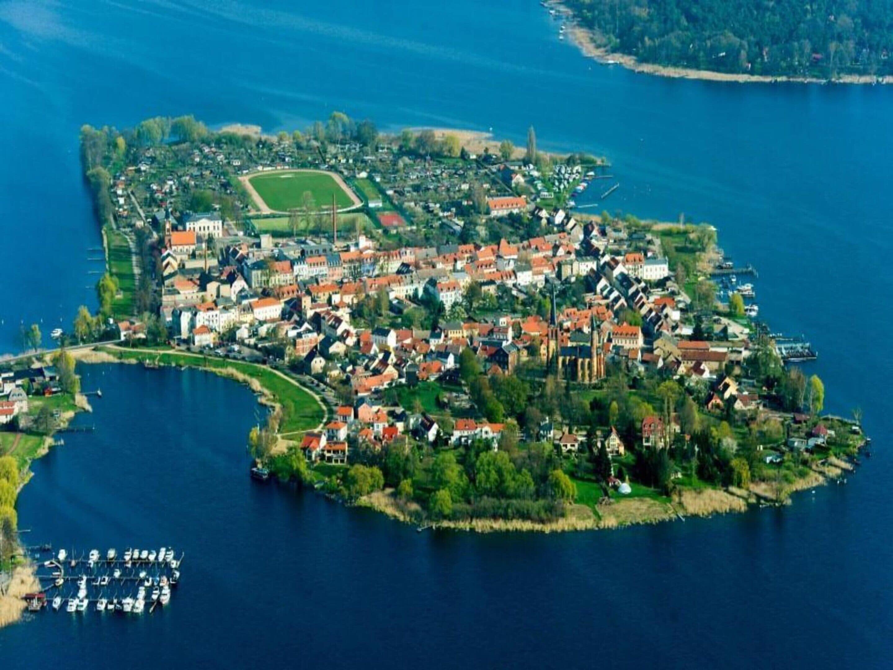 An aerial view of a lakeside residential area with houses, a marina, and a sports field.