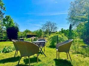 A garden with wicker furniture and a table, surrounded by greenery and trees. - Ferienhaus Havelzeit in Werder an der Havel (Werder (Havel))