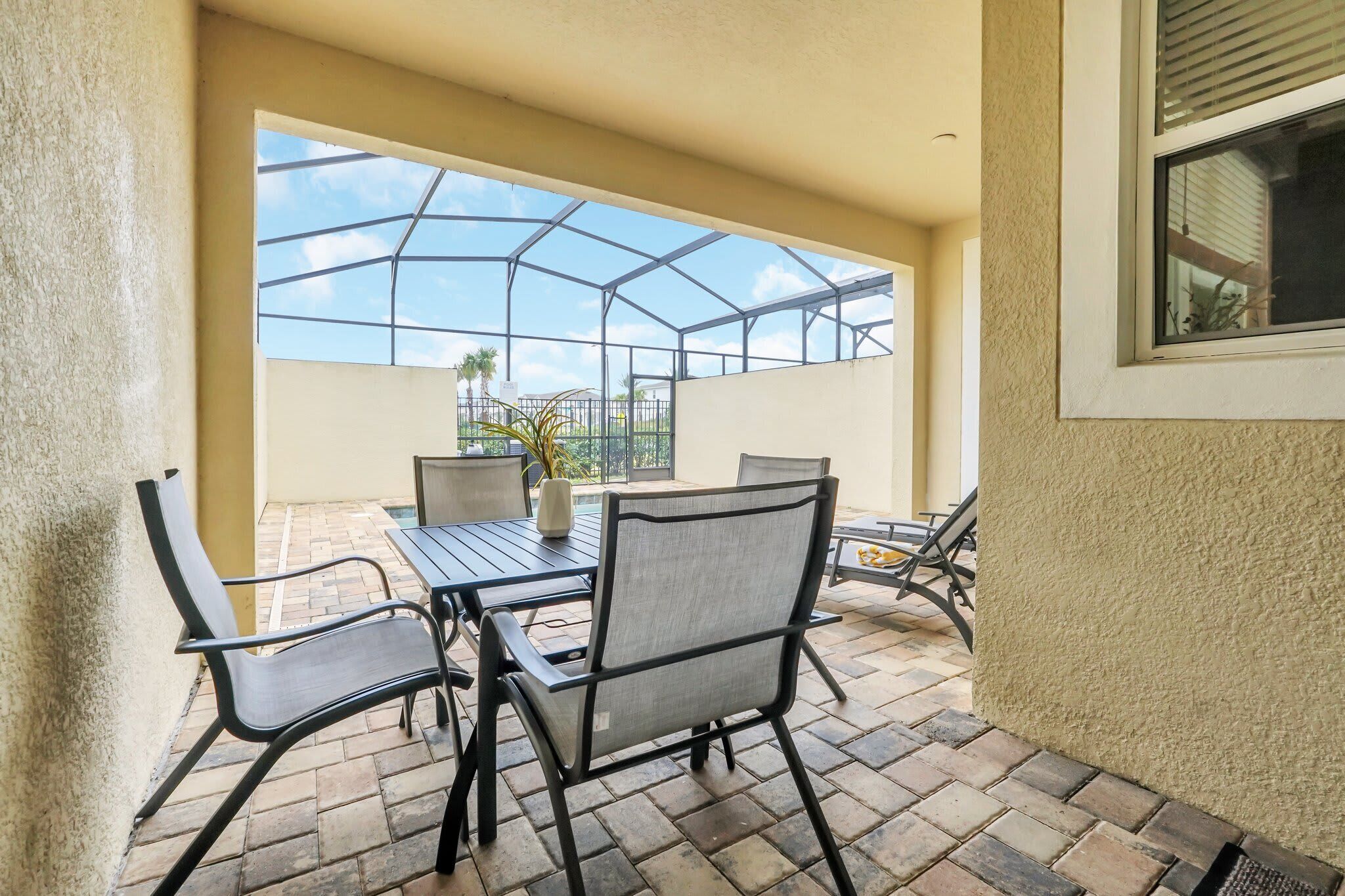 A covered patio area with a table and chairs, a view of the sky through a glass structure, and a potted plant.