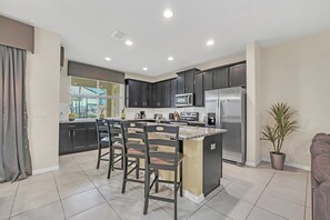 A modern kitchen with dark cabinets, a central island with bar stools, a refrigerator, and a microwave.