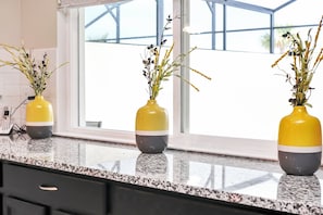 A kitchen counter with three yellow and gray vases containing plants, a window with a view, and a telephone on the counter.
