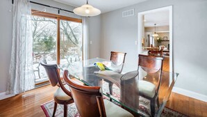 A dining area with a glass table, wooden chairs, and a view through a large window. - ‼️Lovely Ann Arbor Retreat Near Parks & Shops (Ann Arbor)
