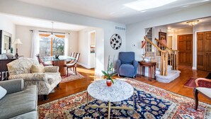 A spacious living room with a round marble coffee table, a dining area with a wooden table and chairs, a blue armchair, and a staircase leading to another level. - ‼️Lovely Ann Arbor Retreat Near Parks & Shops (Ann Arbor)