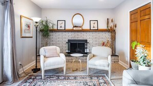 A living room with a fireplace, two white armchairs, a small round table, and a patterned rug. - ‼️Lovely Ann Arbor Retreat Near Parks & Shops (Ann Arbor)