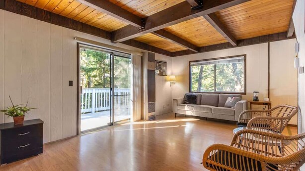 A spacious room with a wooden floor, a sofa, wicker chairs, and a sliding glass door leading to an outdoor area. - ‼️Comfy 2BR Getaway Near Lake Grego w/ Mtn Views (Crestline)