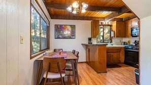 A cozy kitchen with wooden cabinets, a dining table with chairs, and a large window. - ‼️Comfy 2BR Getaway Near Lake Grego w/ Mtn Views (Crestline)