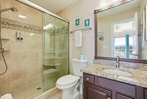 Une salle de bain dotée d’une douche à parois de verre, de toilettes, d’un lavabo avec un plan de toilette en marbre et d’un grand miroir.