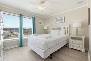 Une chambre d’hôtel avec un lit, des tables de chevet, un ventilateur de plafond et une fenêtre avec des rideaux.