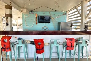 A bar area with turquoise chairs, red life jackets, and a television screen. - Part Time - 3 Bedroom Semi-Oceanfront with Private Hot Tub! (Nags Head)