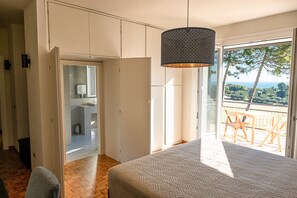 A bedroom with a large bed, a hanging light fixture, a view of the outdoors, and a balcony with chairs. - Bea&Berto | Complete apartment in the hills, a stone's throw from the sea (Marche)