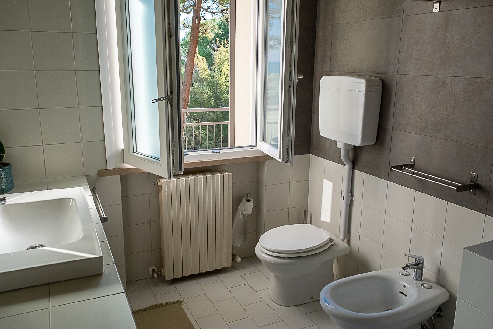 A bathroom with a window, a toilet, a bidet, and a sink.