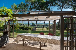 A covered outdoor seating area with a table and chairs, surrounded by a wooden pergola and a view of the landscape. - Bea&Berto | Complete apartment in the hills, a stone's throw from the sea (Marche)