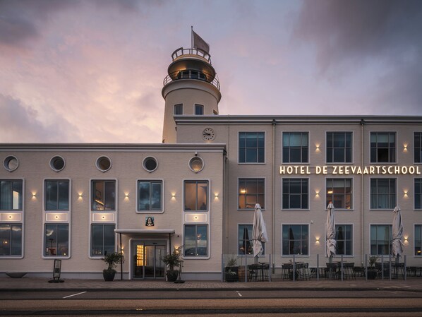 A hotel with a clock tower, a sign reading "HOTEL DE ZEEVAARTSCHOOL", and outdoor seating with umbrellas. - Hotel De Zeevaartschool (Vlissingen)