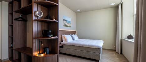 A bedroom with a bed, a wooden wardrobe, a painting on the wall, and a window with curtains.