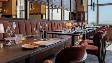 Una larga mesa de comedor con varios asientos, dispuesta con copas de vino, platos y cubiertos.