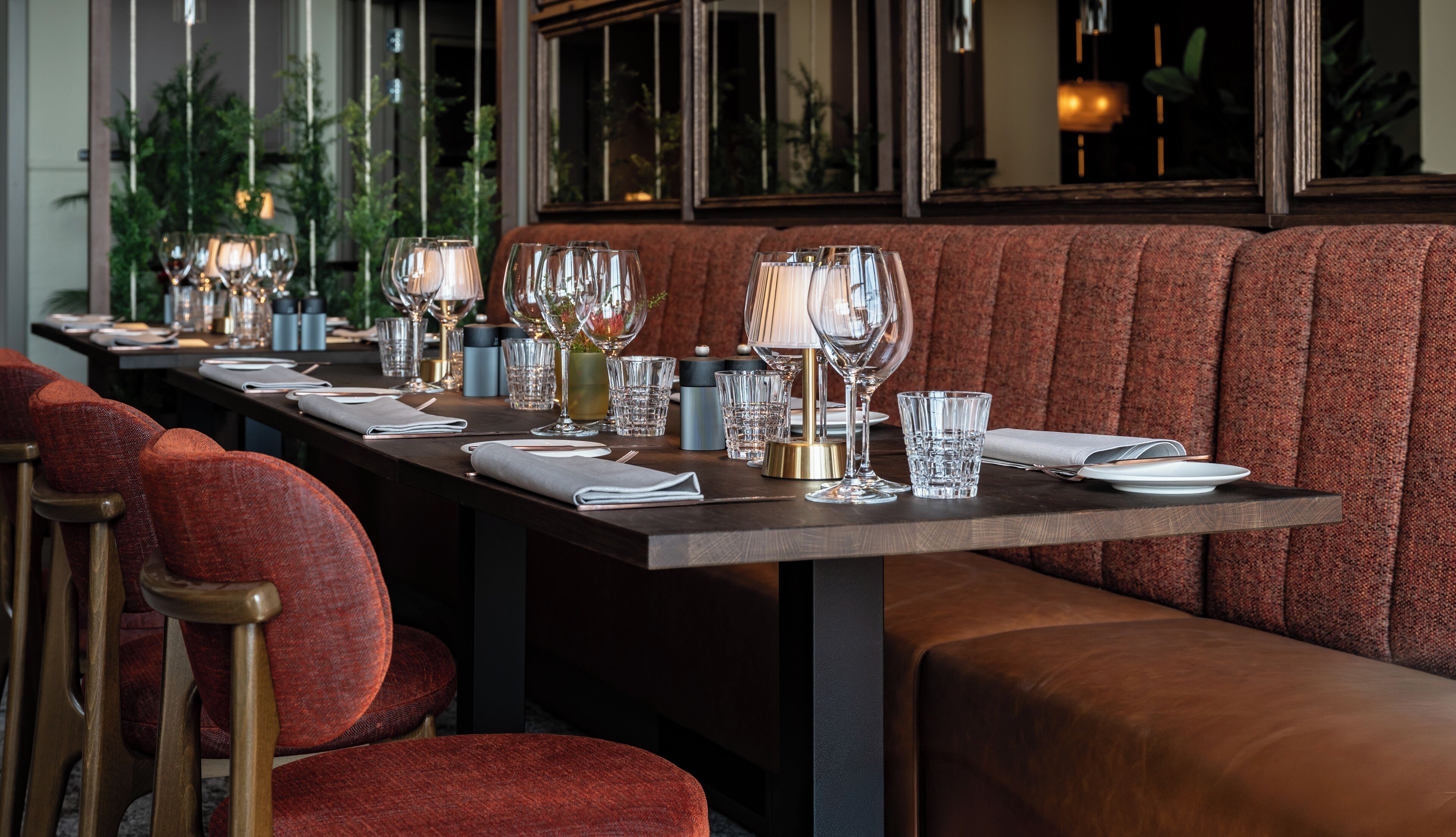 A restaurant with a long table set for dining, featuring red upholstered chairs and a dark wooden table.