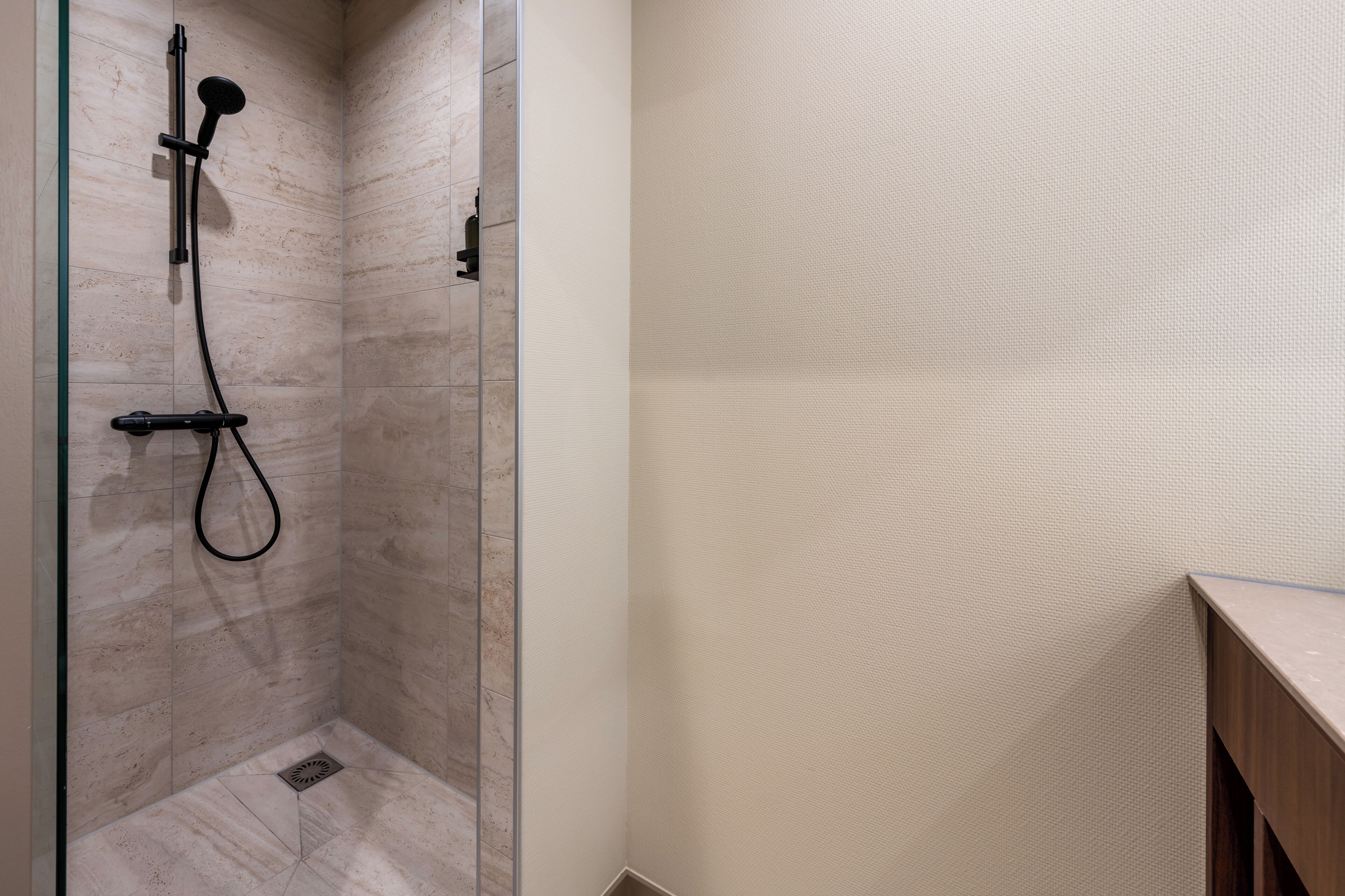 A modern bathroom with a glass-enclosed shower, a wooden vanity, and a textured wall.