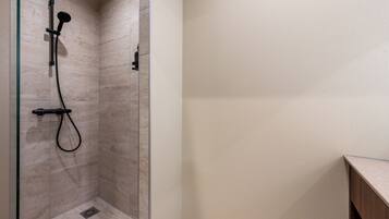 A modern bathroom with a glass-enclosed shower, a wooden vanity, and a textured wall.