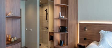 A modern hotel room with a wooden wardrobe, a walk-in closet, a shower area, and a neatly made bed.