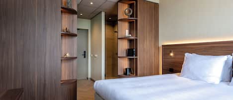 Habitación de hotel con una cama grande, armario de madera y estantes empotrados con varios objetos.