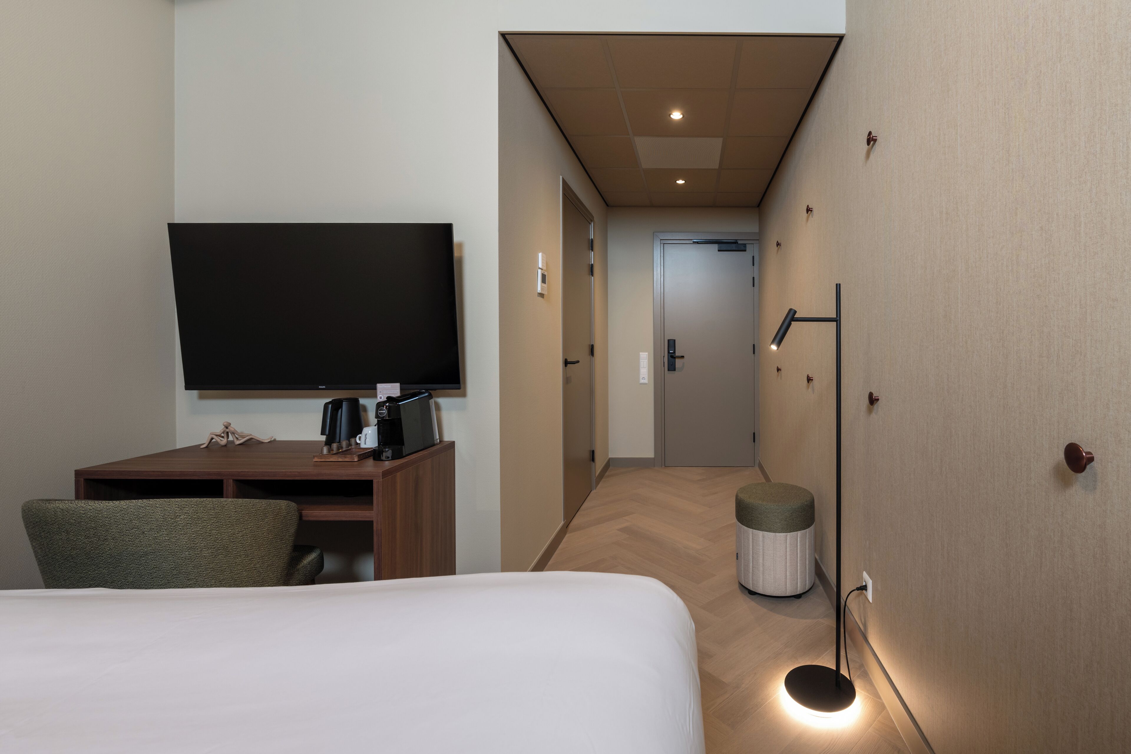 Une chambre d’hôtel comprenant un lit, un bureau avec un téléviseur à écran plat, une chaise, une poubelle et une lampe de sol.