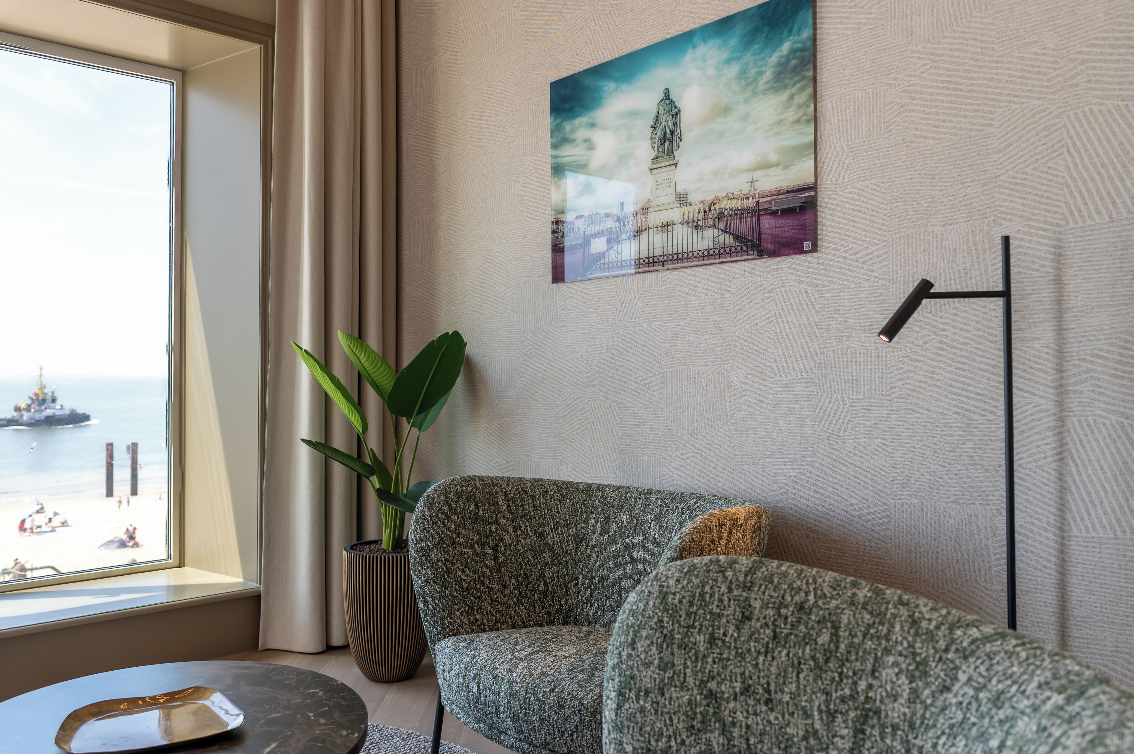 Una habitación con vista al mar, una pintura de una estatua, una planta verde y una lámpara de pie moderna.