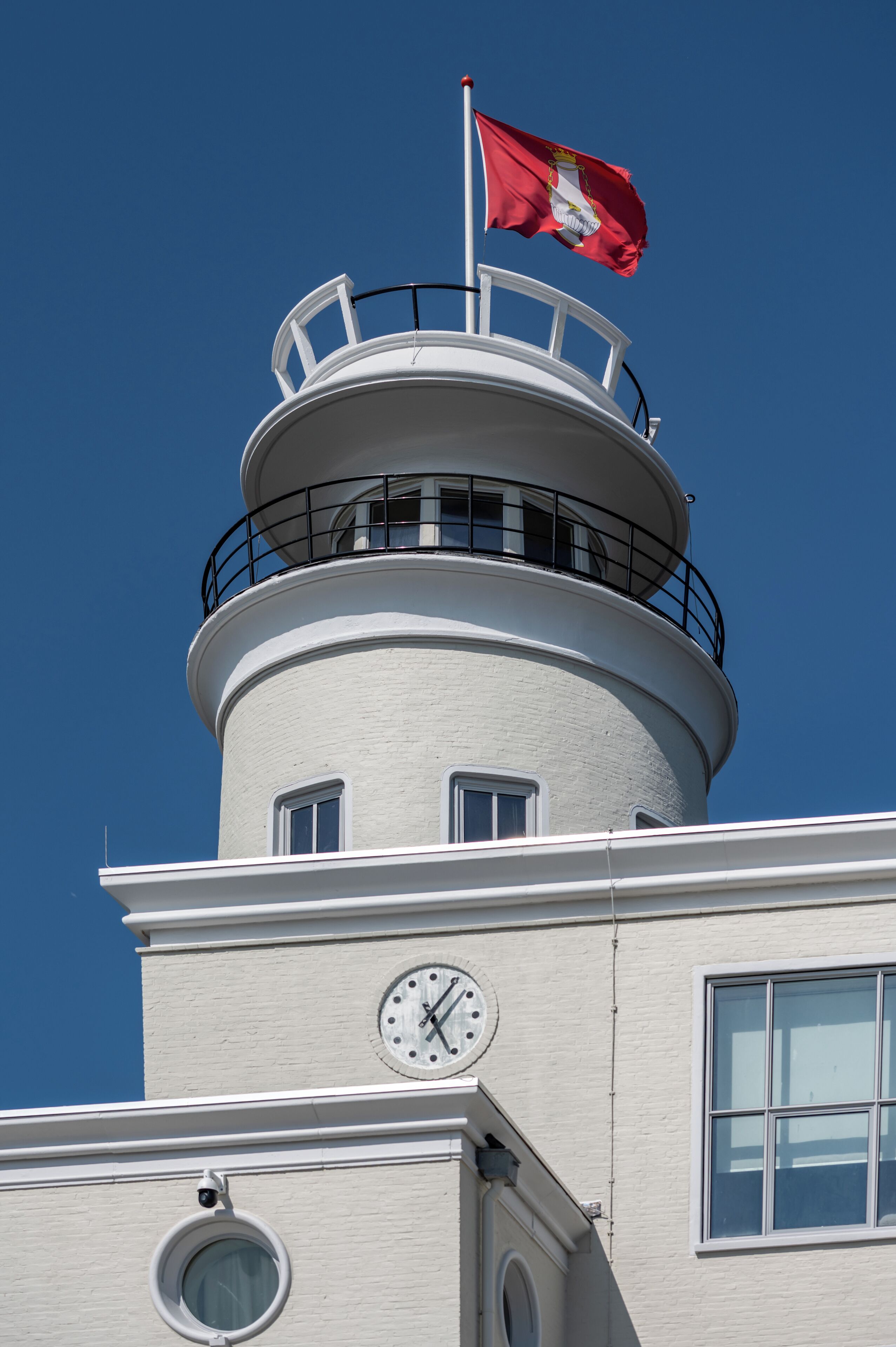 A lighthouse with a clock and a flag on top.