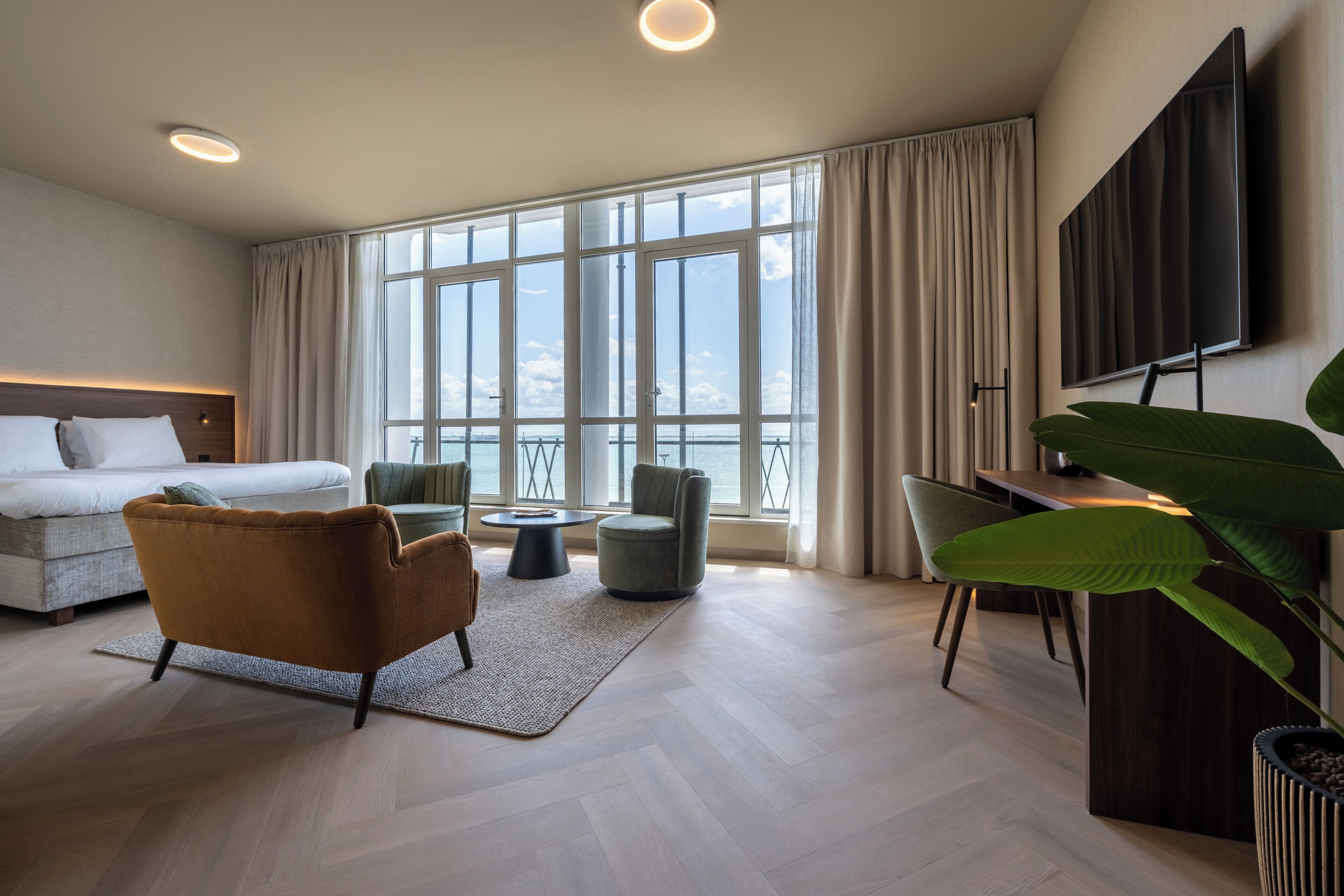 Una habitación de hotel moderna con un ventanal grande, una cama, un sofá, un escritorio y un televisor.