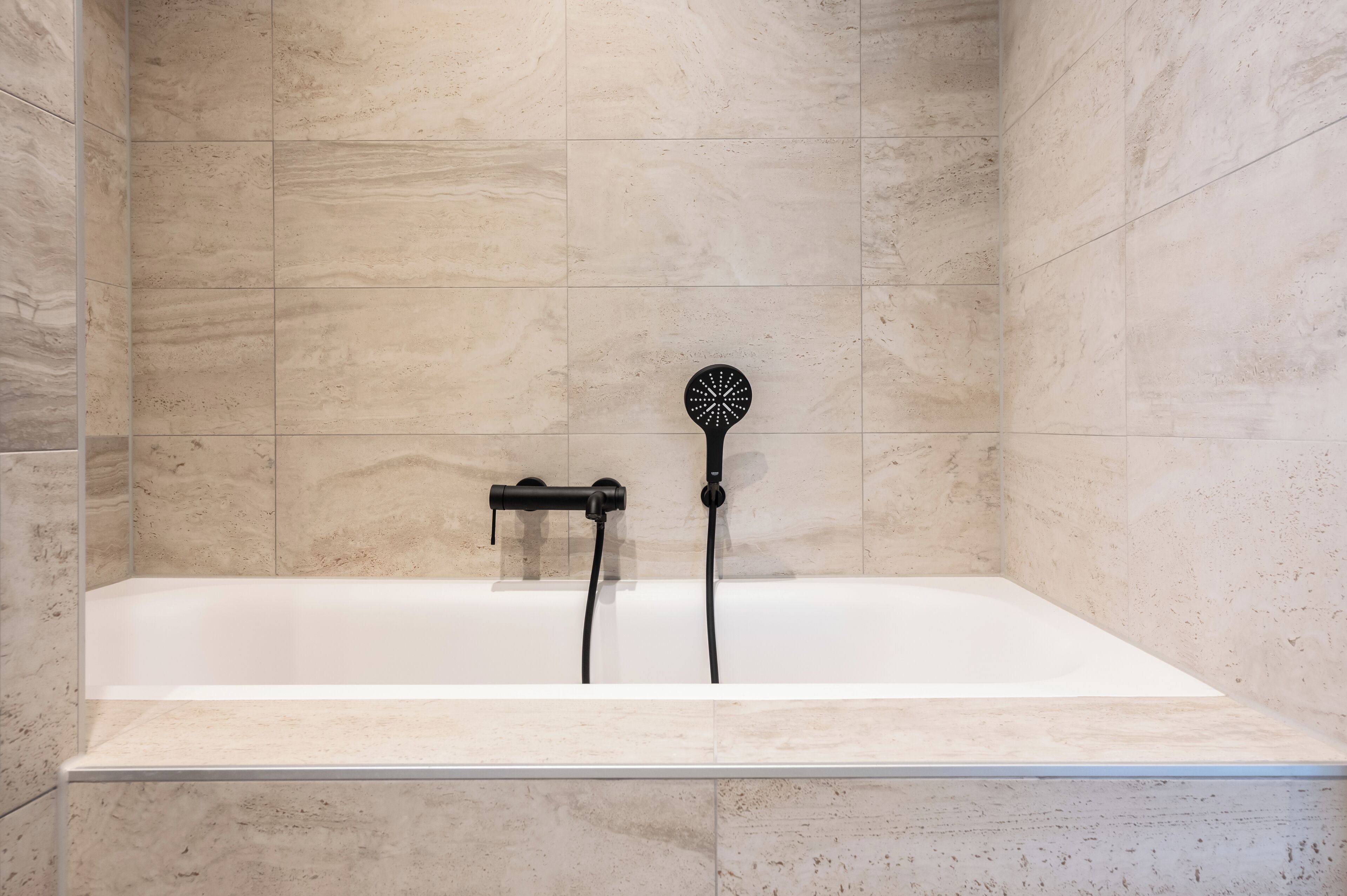 A modern bathroom with a white bathtub, a handheld showerhead, and a wall-mounted faucet.