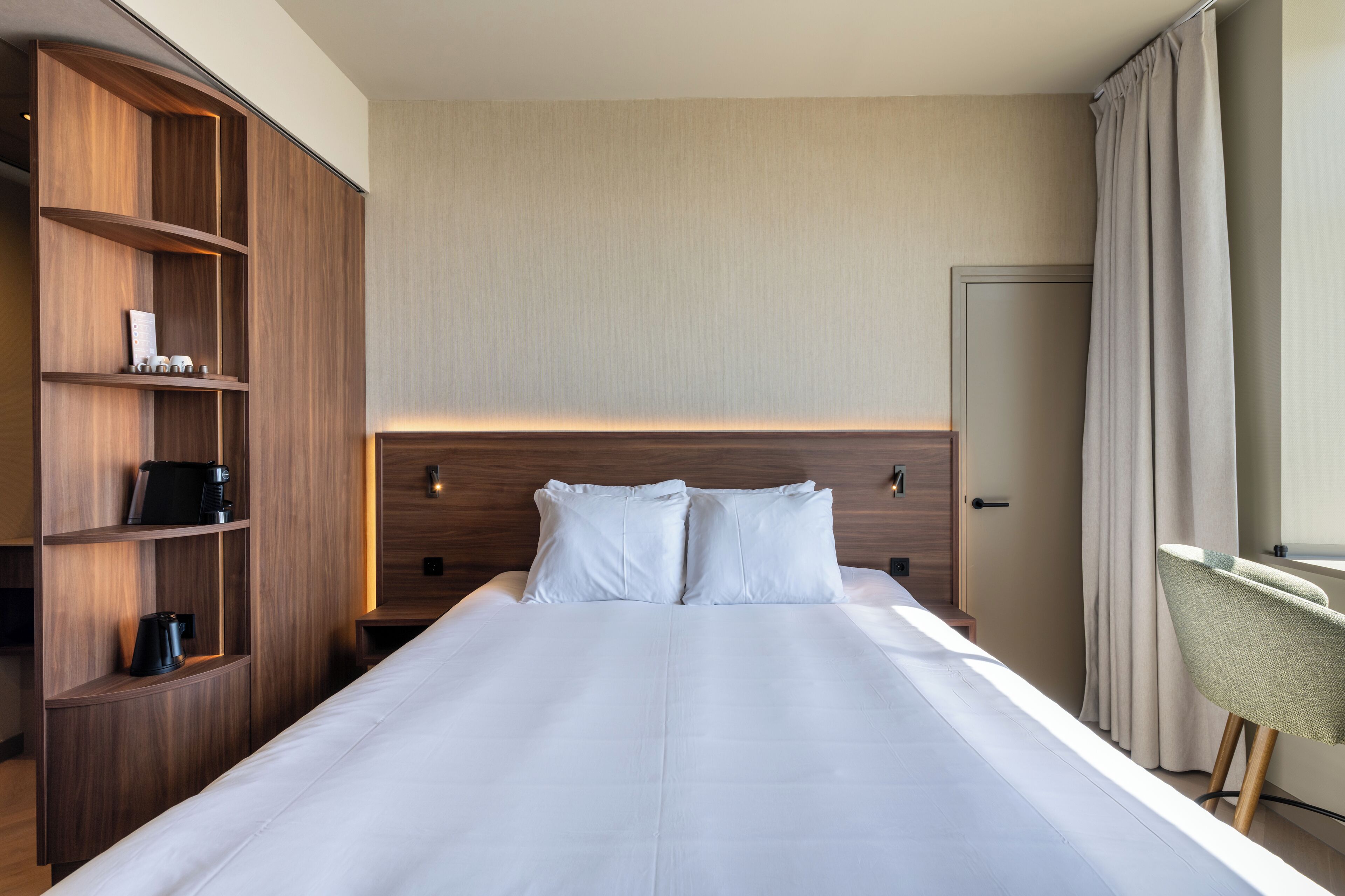 Een hotelkamer met een groot bed, houten hoofdeinde, een ingebouwde boekenkast en een bureau met stoel.